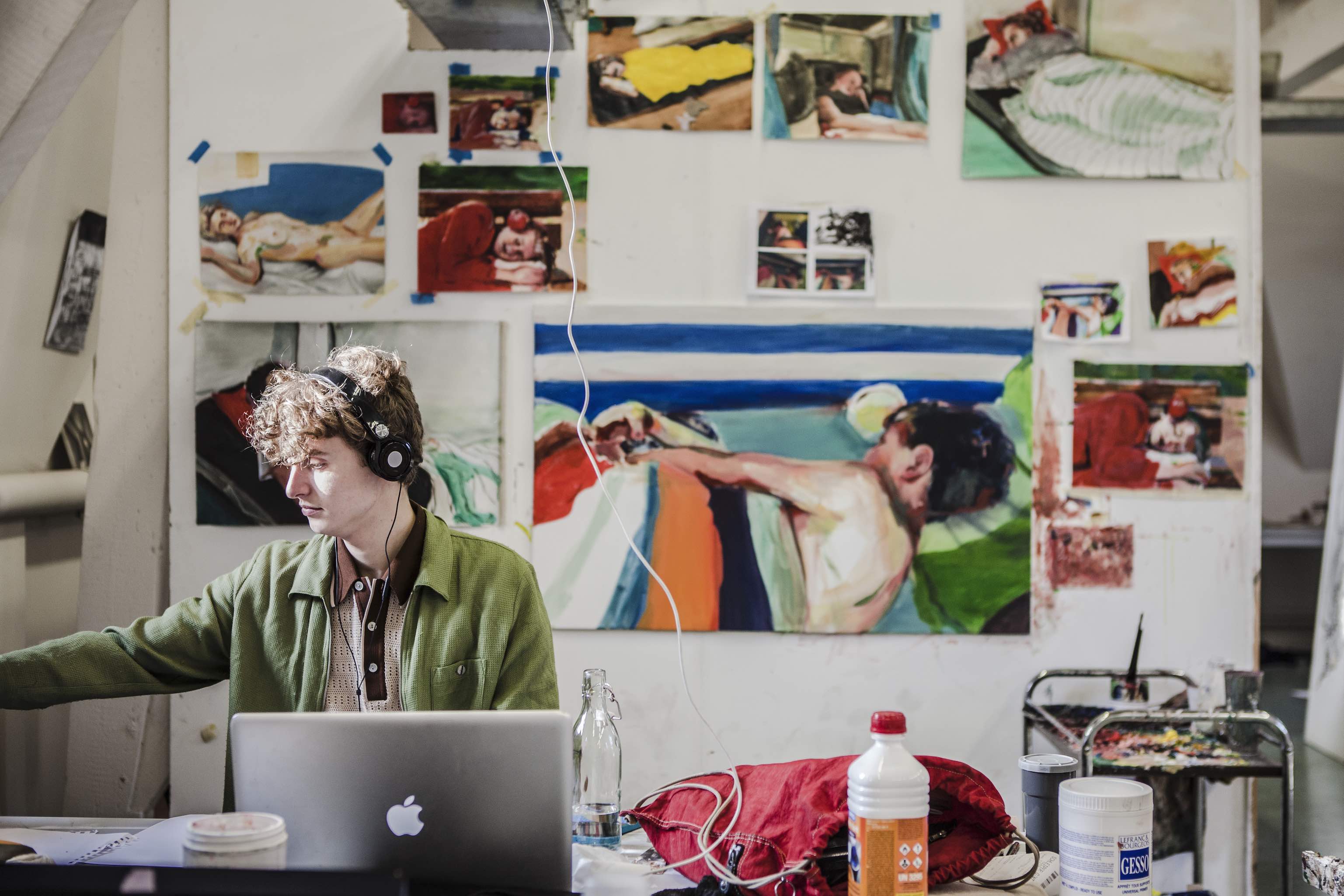 Pieter zitten met koptelefoon aan het werk voor muur met schilderijen van liggende mensen