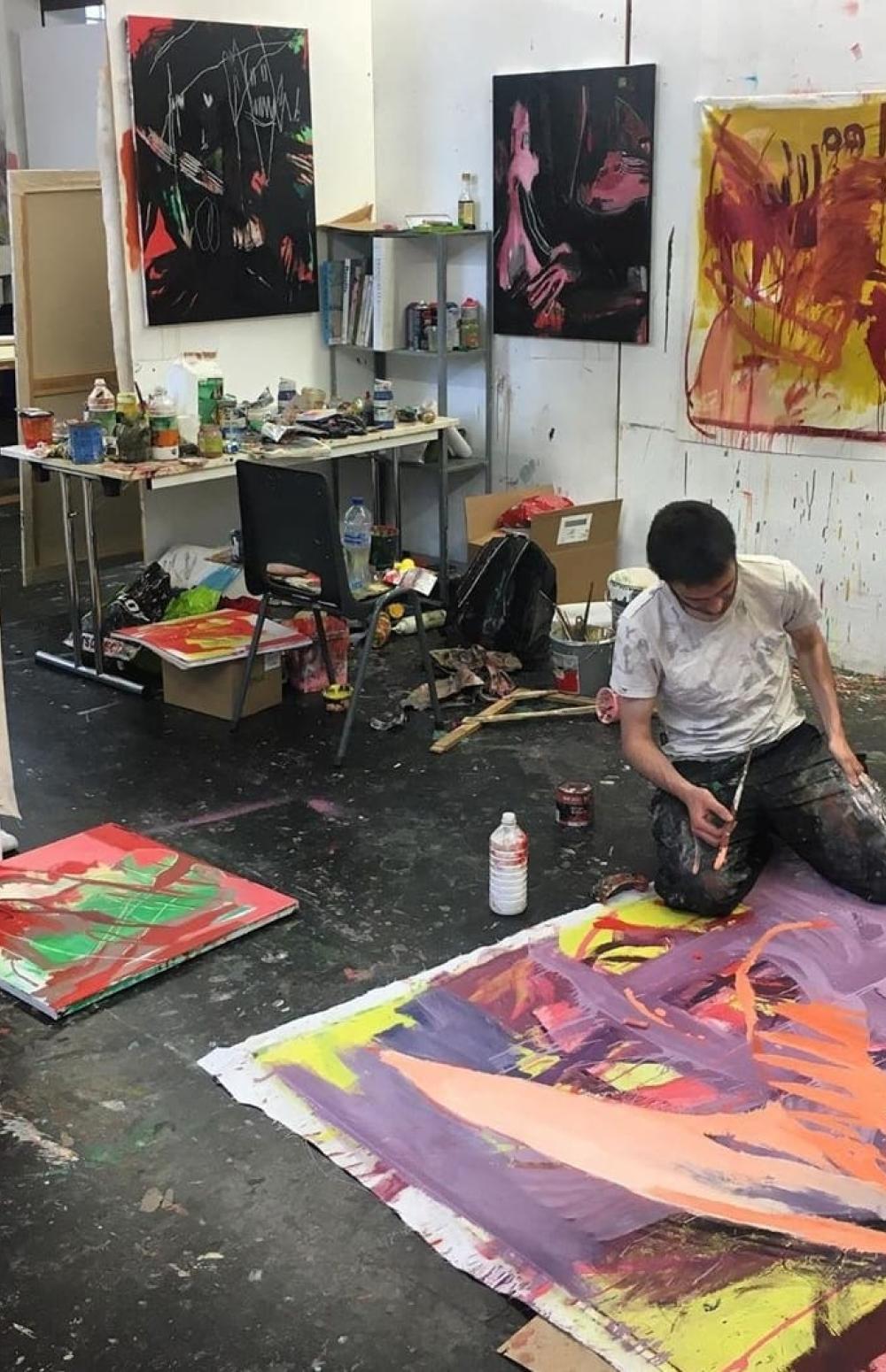 Arthur Defoor zittend op de knieën aan het werk in zijn atelier rondom zijn schilderijen.